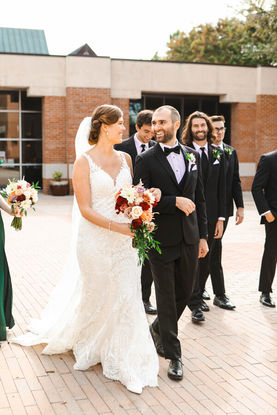 Bride and groom walk towards the camera surrounded by their friends. They lovingly gaze into each other's eyes and smile.