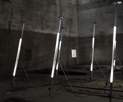 Oh My God by LAb[au], with illuminated tubes mounted on tall tripods and cables across the floor in a dark concrete interior.