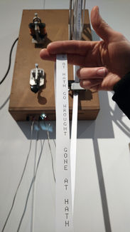 Hand holding a paper strip with printed letters in front of a telegraph panel.