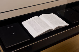 Open book beneath a transparent cover on a black display case.