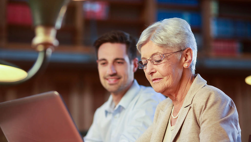 Eine ältere Dame mit weißen Haaren sitzt vor einem Labtop. Dahinter zu erkennen eine Person der jüngeren Generation schaut ebenso freudvoll auf den Labtop