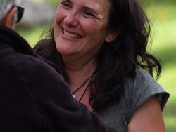 Une femme sourit à une autre face à elle. Celle de dos à les cheveux courts et blancs, elle porte des lunettes noires et une veste noire. La personne qui sourit est en tee-shirt kaki manches courtes, elle a les cheveux bruns foncés et longs, ondulés.