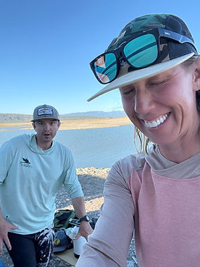 Smiling woman and man outdoors near a lake.