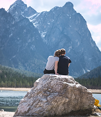 Couple sitting on a rock overlooking mountains and lake