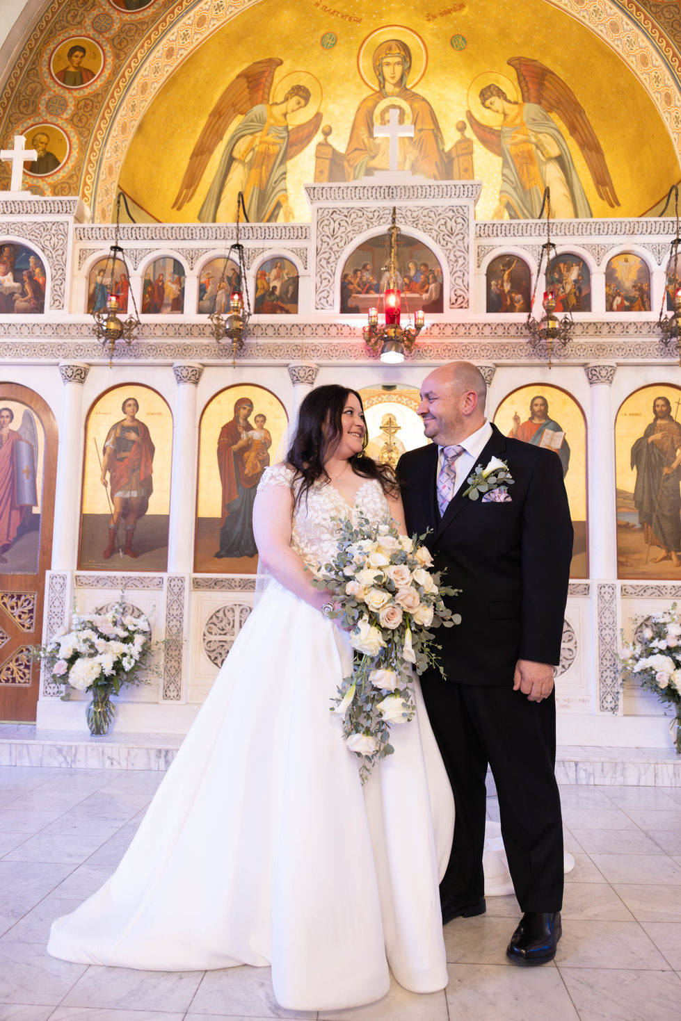 Newlyweds at ornate Orthodox church ceremony with golden Byzantine icons backdrop