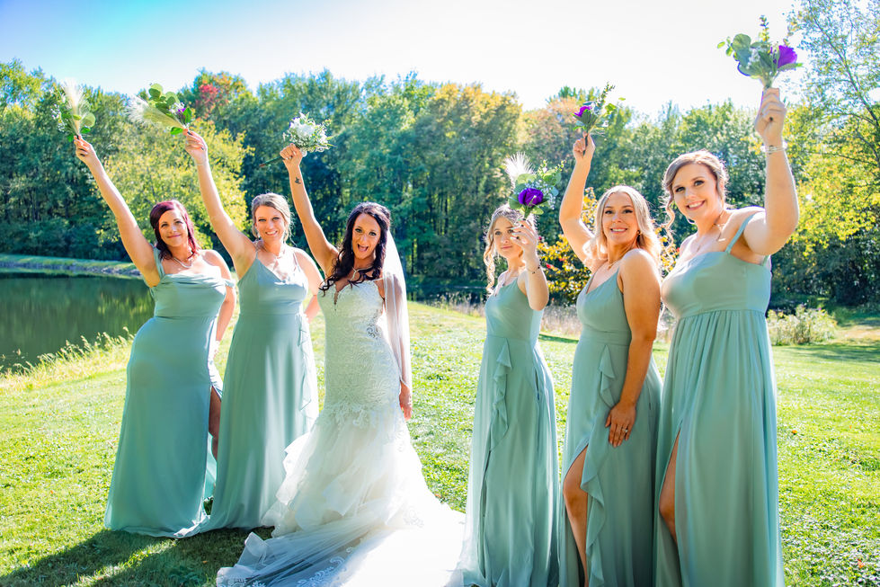 Bride and bridesmaids in sage bridesmaid dresses celebrating with bouquets raised outdoors
