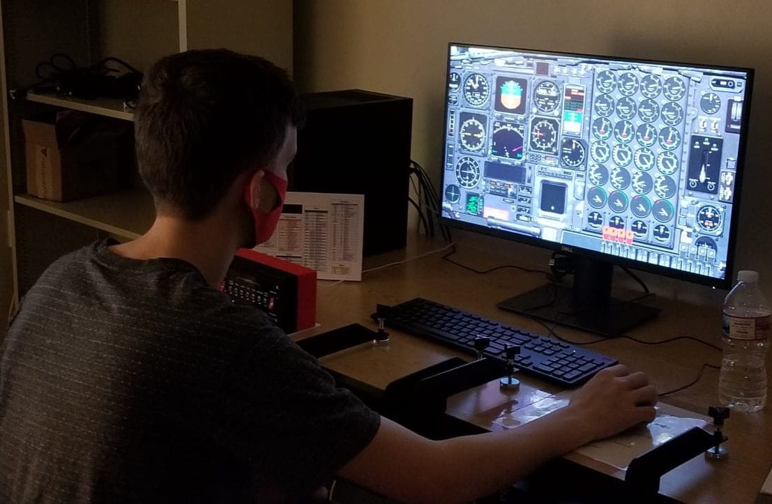 A student sitting at the flight simulator on the computer, looking at the screen with airplane cockpit controls.