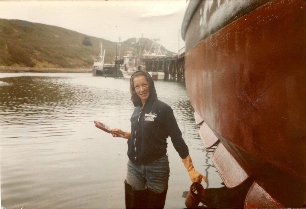 Pam putting bottom paint on a boat at low tide, Sand Point, Alaska.