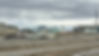 Utqiaġvik in early June: an aluminum whaling boat parked in the gravel where a road becomes a working yard, the blue clapboard church in the middle distance, low houses trailing off toward the lagoon. The town is not decoration around the culture; it is the culture’s working perimeter. Photograph by John J. King II.