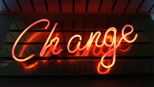 Neon sign displaying the word "Change" in vibrant orange-red hues against a dark background, evoking a mood of transformation.