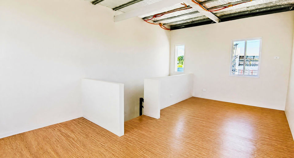 Bright modern upper‑floor room with wooden flooring, white walls, windows, and exposed ceiling structure.