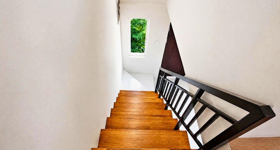 Modern indoor staircase with wooden steps, black railing, white tile landing, and natural light from a window.