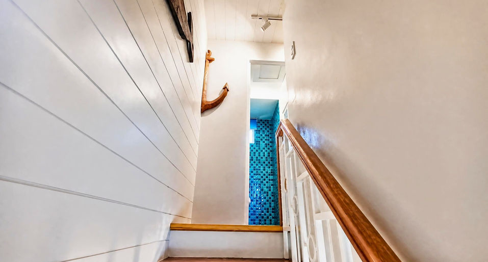 Staircase interior of the Cara House Model in Camella Capas with white walls, wooden handrail, nautical anchor décor, and blue mosaic tiles on the upper landing.