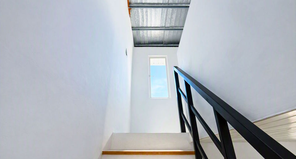 Indoor staircase with wooden-edged steps, black handrail, and natural light from a small window.