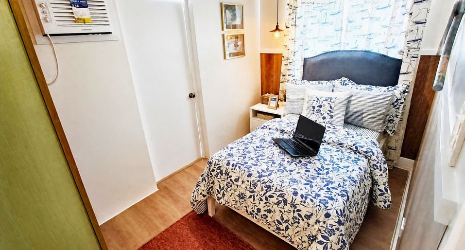 Single bedroom in the Cara House Model at Camella Capas with blue floral bedding, nautical curtains, bedside décor, and warm wooden flooring.