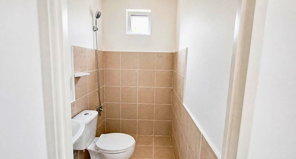 Compact fully finished bathroom with beige tiles, toilet, handheld shower, and natural light in a Camella Capas home.