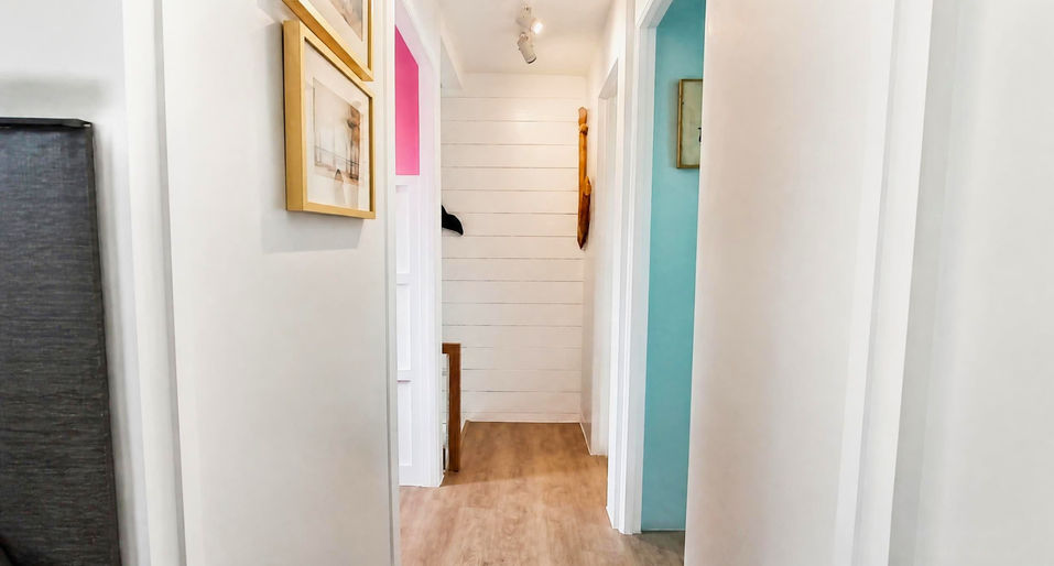 Bright hallway in the Cara House Model at Camella Capas with white walls, wood flooring, gold‑framed décor, and colorful accent doorways.