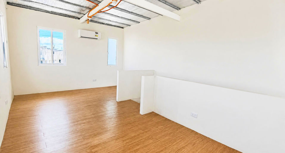 Bright modern room with wooden flooring, light walls, windows, exposed ceiling, and air‑conditioning unit.