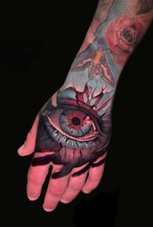 Color realistic tattoo of an eye on a hand created by Albert Gajewski at Ink Tattoo Basel – expressive red and blue tones with symbolic design.