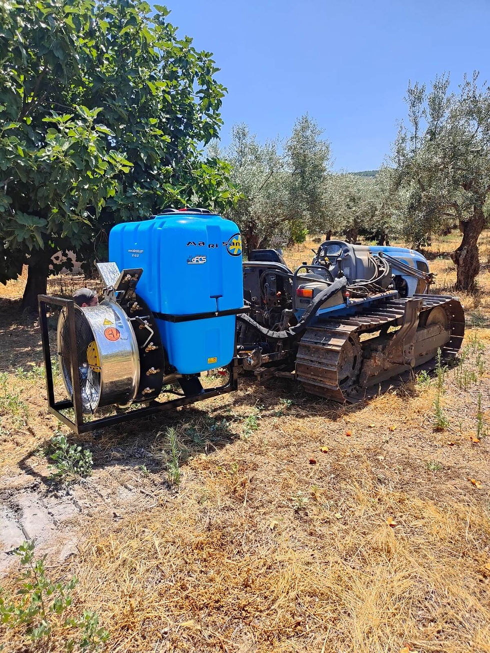 Tractor de orugas con atomizador azul en campo agrícola