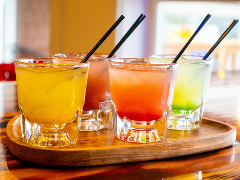 Colorful cocktails in glasses placed on a wooden tray with straws and ice