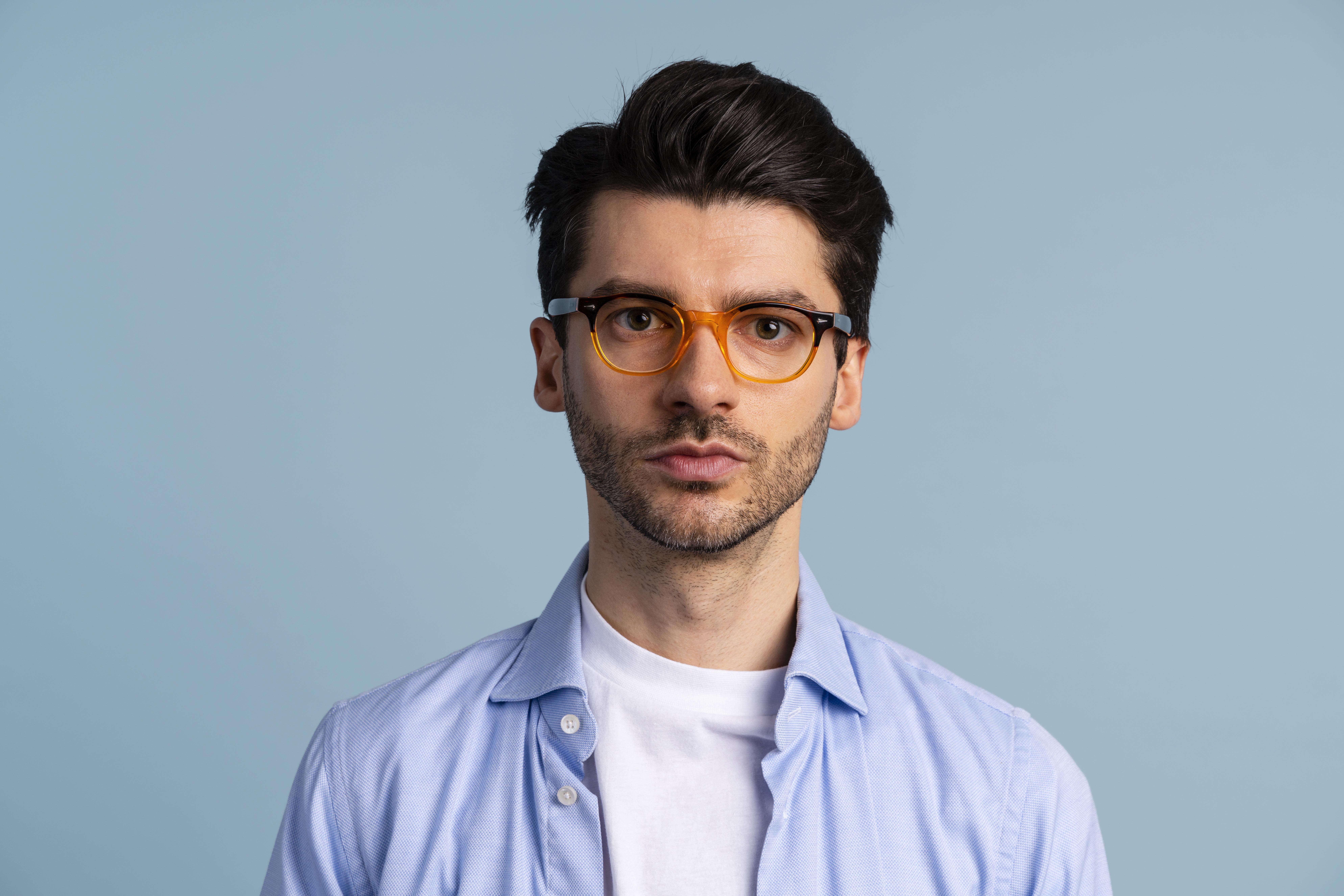 Man with dark hair, beard, orange glasses, and blue shirt