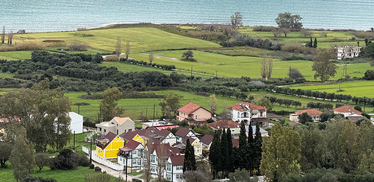 View over Livadi Bay in Kefalonia with villas, farmland, and mountains in the distance
