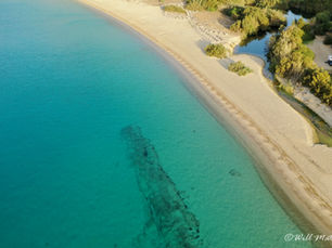 Luchtfoto van een zandstrand, turquoise zee en een kleine rivier met begroeiing erlangs op Sardinië.
