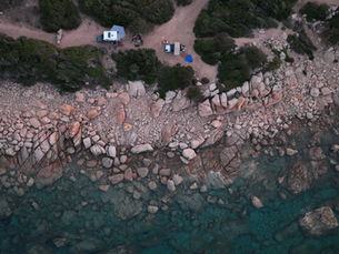 Luchtfoto van de rotsachtige kust van Sardinië, met voertuigen bij de zee.