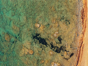 Luchtfoto van een voertuig met caravan aan een rotsachtige kust met helder turquoise water.
