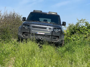 Een donkere 4x4 op een grasweg tussen hagen, onder een blauwe lucht.
