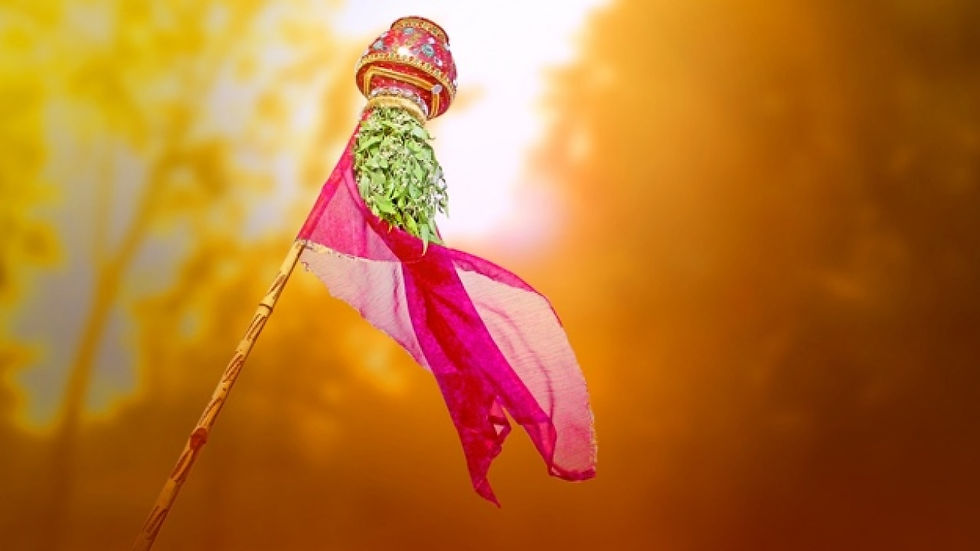 A decorated bamboo pole with a pot, green leaves, and a red cloth against a warm, golden background, evoking festivity and tradition.