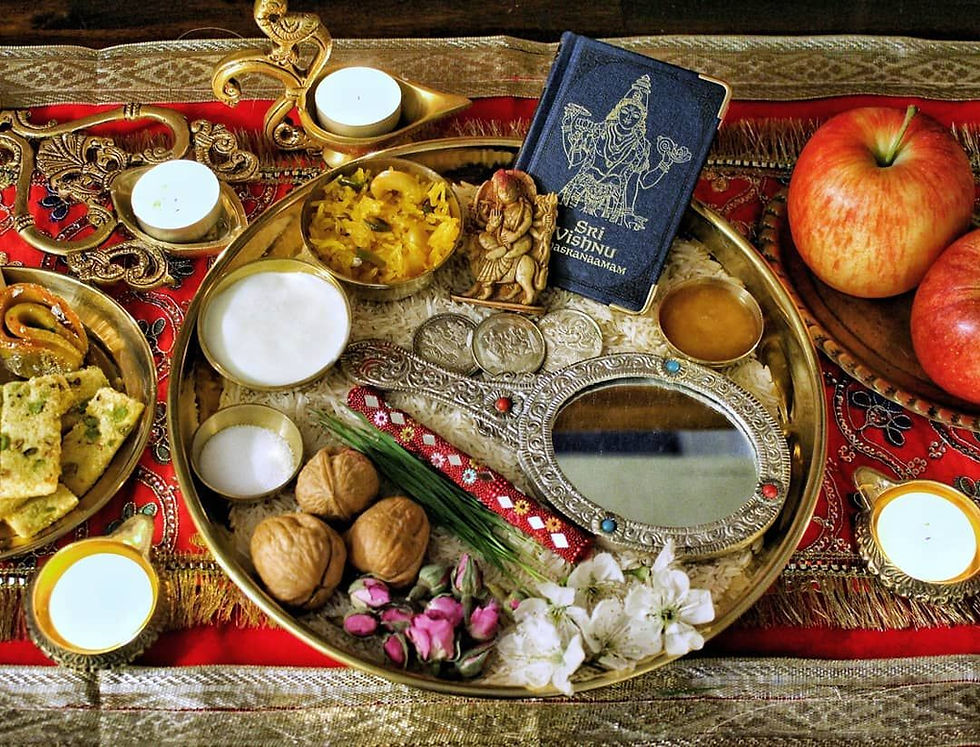A festive Hindu offering setup with a brass plate, sweets, nuts, flowers, candles, a "Sri Vishnu" book, and apples on a decorative red cloth.