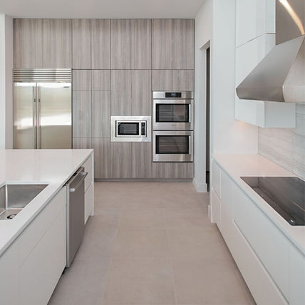 Modern kitchen with light wood cabinets, stainless steel appliances, white countertops.
