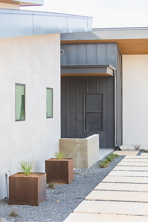 Modern home exterior features concrete walls, metal siding, stone path, planters.