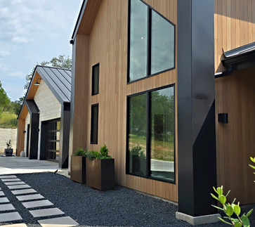 Modern house with wood siding, large windows, and gravel driveway.