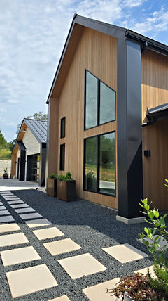 Modern house with wood siding, large windows, and gravel driveway.