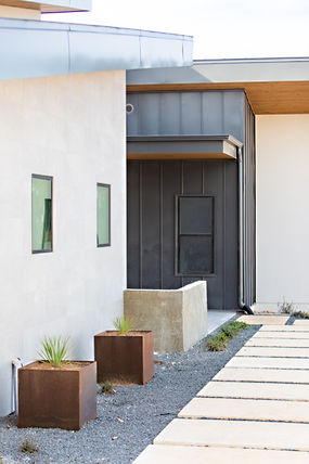 Contemporary house entrance, white wall, dark siding, planters, concrete walkway.