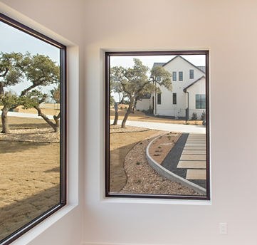 View of modern white house, driveway, and trees through windows