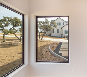 Modern white house through windows with winding driveway and trees.