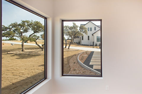 View of modern white house, driveway, and trees through windows