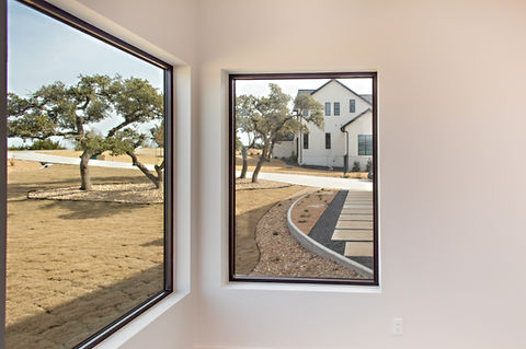 Modern windows frame a house exterior, driveway, landscaping, and mature trees.