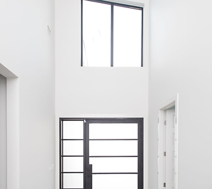 Modern entryway with tall white walls, large black door, and high window.