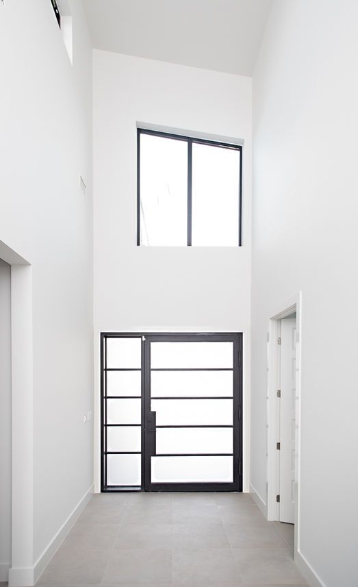 Modern entryway with tall white walls, black door, and large window.
