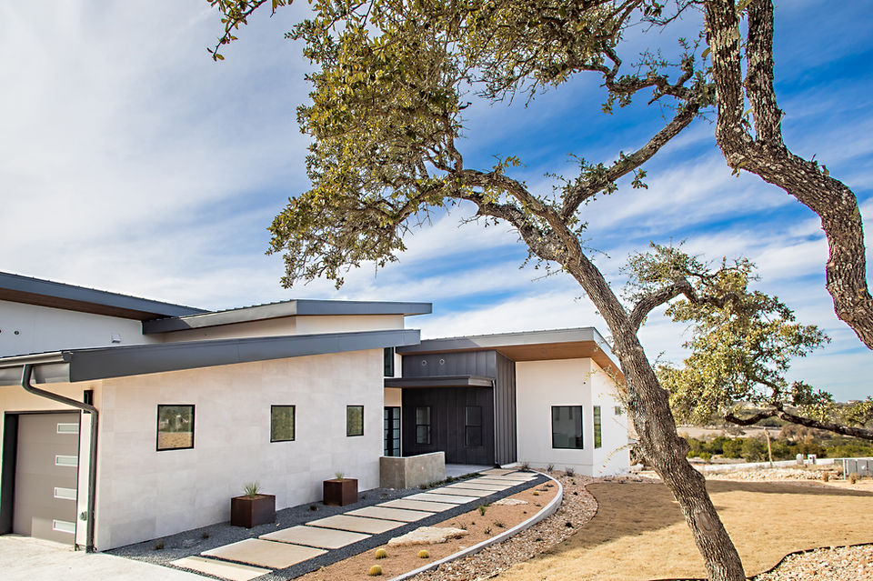 White modern home, dark entry, sleek pathway, large tree, blue sky.