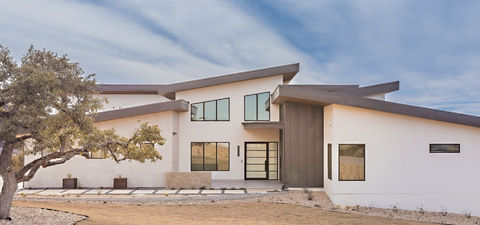 Contemporary white stucco house, angular roof, large windows, desert setting.