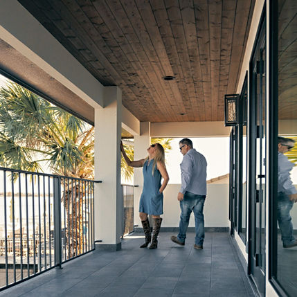 Man and woman on modern balcony with wooden ceiling and palm tree.