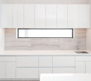 Modern white kitchen cabinetry with a narrow rectangular window over a sink.