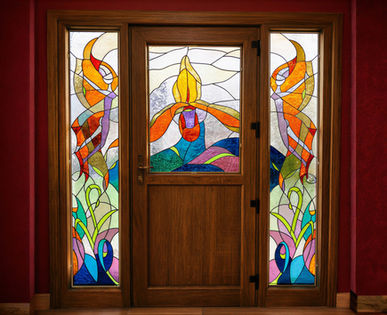Vitrail de porte d'entrée aux motifs floraux abstraits colorés — orangés, verts, bleus et violets — encadrant une porte en bois, deux panneaux latéraux assortis