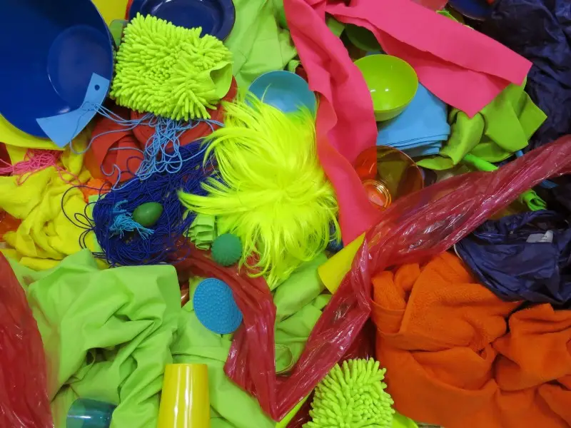 Conjunto de objetos e tecidos em cores neon espalhados sobre uma superfície, incluindo tigelas, fios, panos e elementos texturizados.